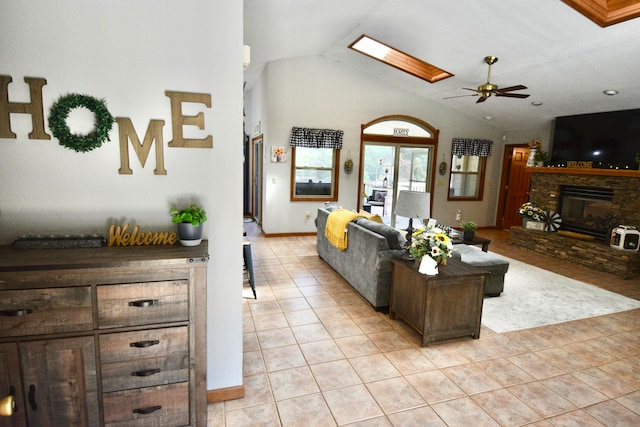 tiled living room featuring ceiling fan, a stone fireplace, and lofted ceiling with skylight