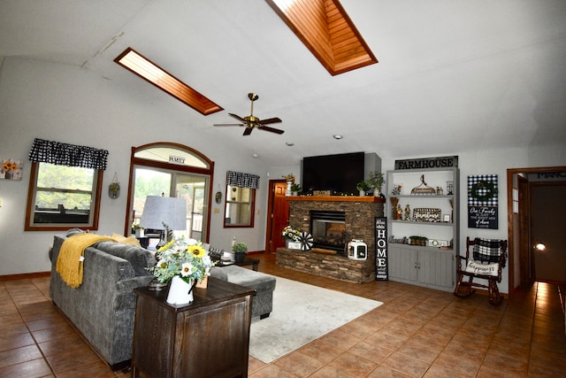 tiled living room featuring ceiling fan, a stone fireplace, and vaulted ceiling with skylight