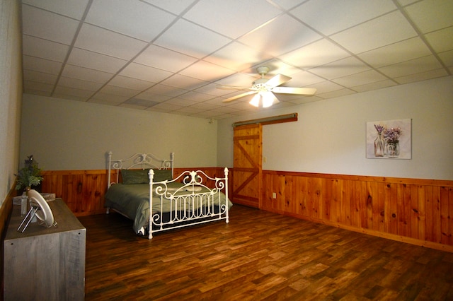 bedroom with a drop ceiling, wooden walls, ceiling fan, and dark hardwood / wood-style flooring