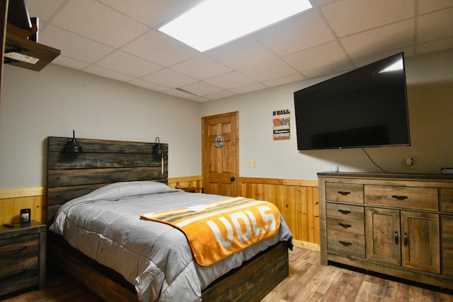 bedroom featuring a drop ceiling, wooden walls, and light hardwood / wood-style floors