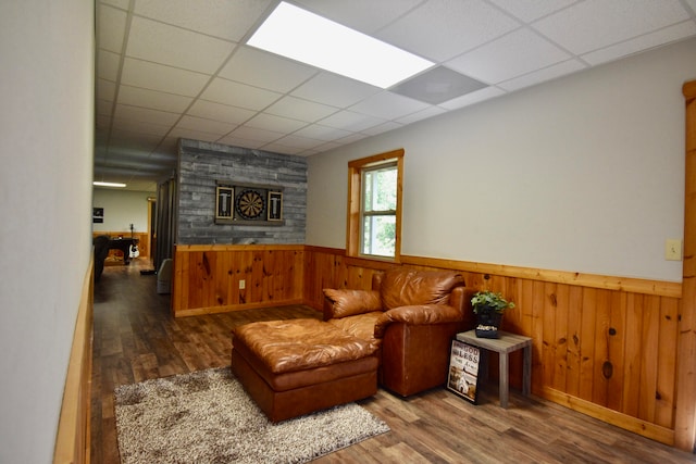 living room featuring wood-type flooring, wooden walls, and a paneled ceiling