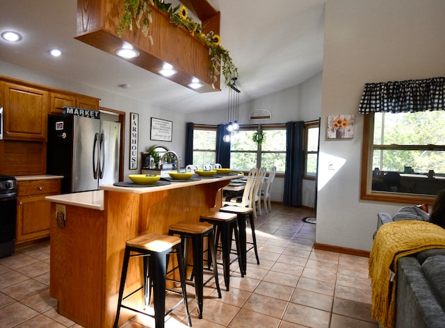 kitchen featuring a kitchen breakfast bar, stainless steel refrigerator, light tile patterned floors, lofted ceiling, and a center island