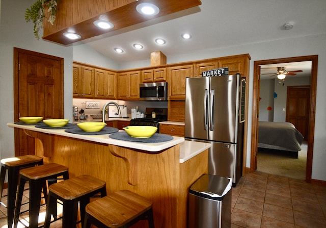 kitchen featuring appliances with stainless steel finishes, vaulted ceiling, dark tile patterned flooring, a breakfast bar area, and ceiling fan