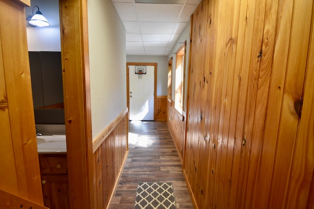 corridor featuring wooden walls, a drop ceiling, and dark wood-type flooring