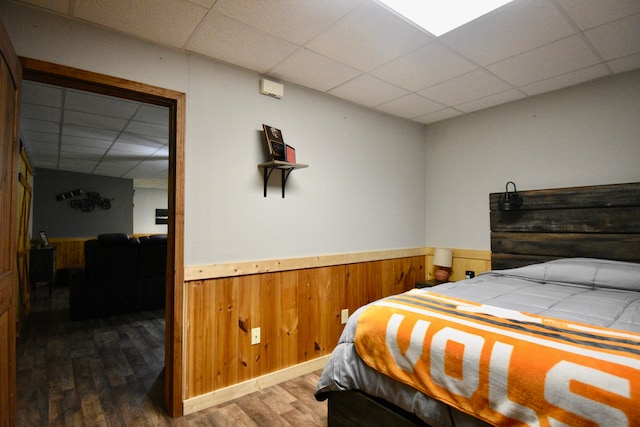 bedroom with a drop ceiling, wood walls, and dark hardwood / wood-style flooring