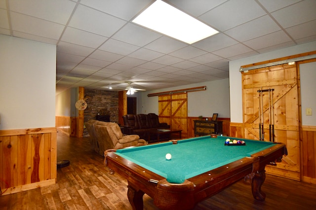 playroom with billiards, a barn door, wood walls, wood-type flooring, and a drop ceiling