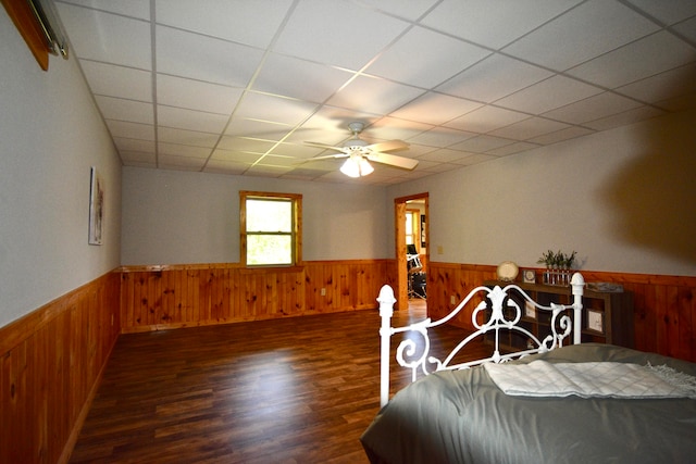 bedroom featuring a drop ceiling, wood walls, ceiling fan, and dark wood-type flooring