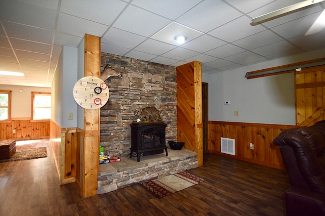 living room featuring wooden walls, dark hardwood / wood-style floors, a wood stove, and a paneled ceiling