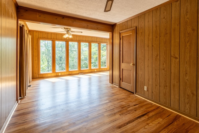 unfurnished room featuring a textured ceiling, wood walls, ceiling fan, and light hardwood / wood-style flooring