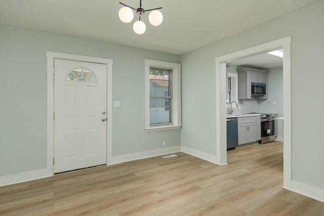 foyer entrance featuring light wood-type flooring, a notable chandelier, and sink