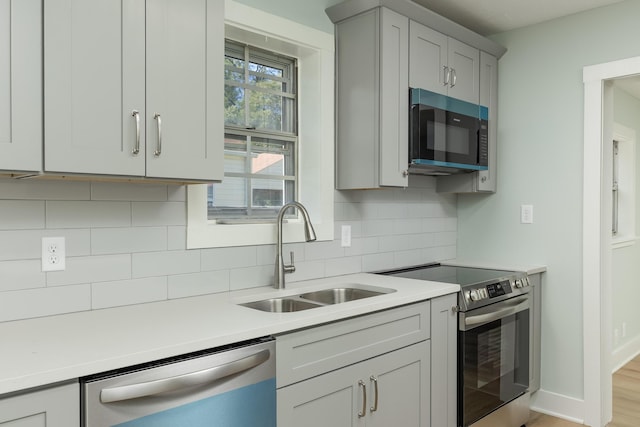 kitchen featuring sink, gray cabinets, decorative backsplash, appliances with stainless steel finishes, and light wood-type flooring