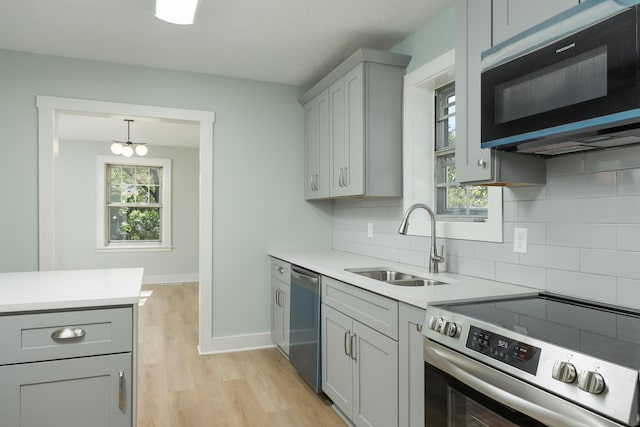 kitchen featuring sink, stainless steel appliances, gray cabinets, decorative backsplash, and light wood-type flooring