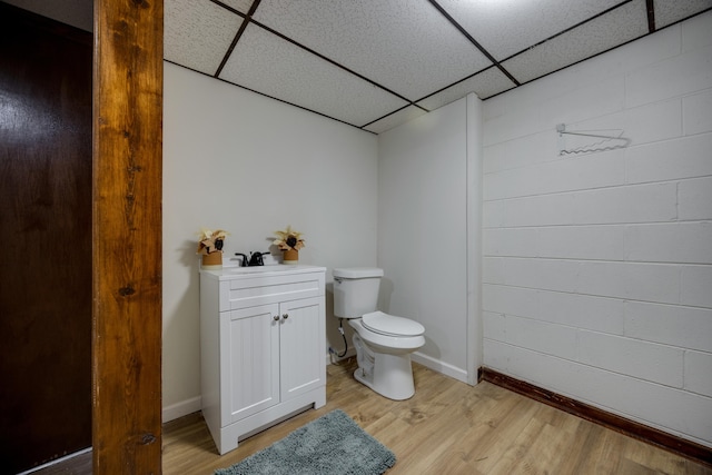 bathroom with wood-type flooring, vanity, toilet, and a drop ceiling