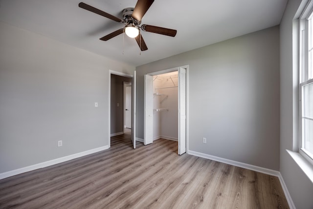 unfurnished bedroom with ceiling fan, a closet, a spacious closet, and light wood-type flooring