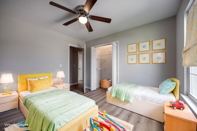 bedroom featuring a spacious closet, ceiling fan, wood-type flooring, and a closet