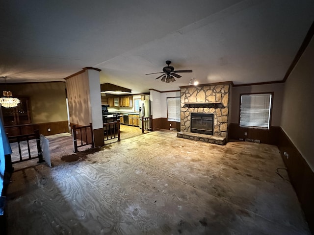 living room featuring ceiling fan, lofted ceiling, ornamental molding, wooden walls, and a fireplace