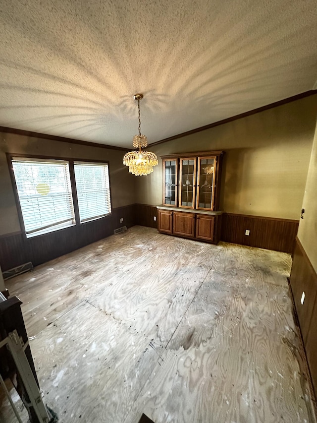 unfurnished dining area with ornamental molding, a notable chandelier, vaulted ceiling, and a textured ceiling