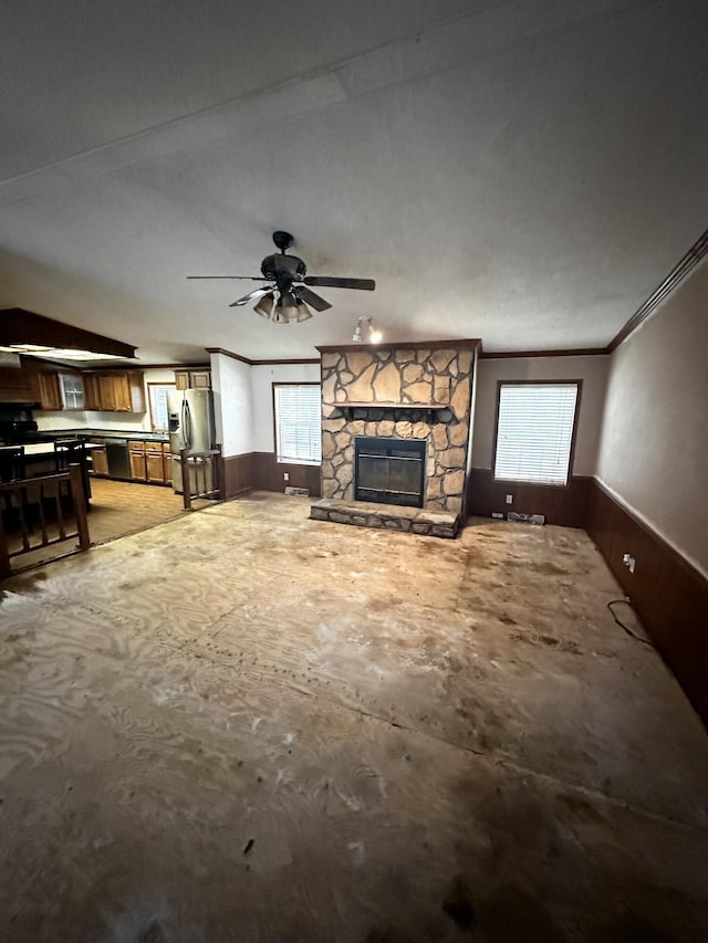 unfurnished living room with a stone fireplace, ornamental molding, ceiling fan, and plenty of natural light