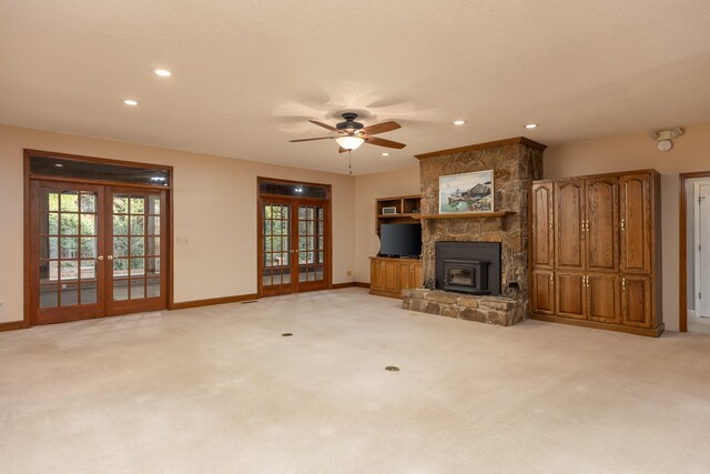 unfurnished living room featuring french doors, light colored carpet, a wood stove, and ceiling fan