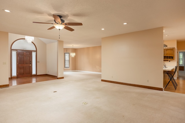 unfurnished living room featuring a textured ceiling, ceiling fan with notable chandelier, and light colored carpet