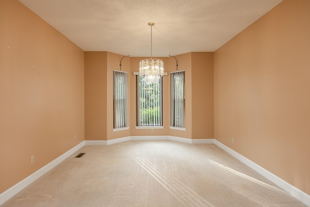 carpeted empty room featuring a chandelier and a textured ceiling