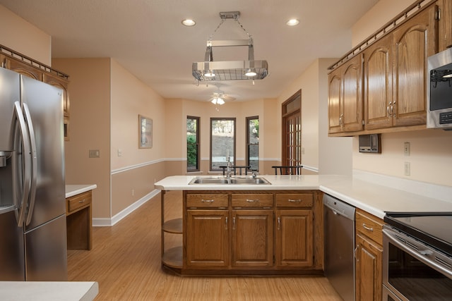 kitchen with light wood-type flooring, sink, kitchen peninsula, appliances with stainless steel finishes, and ceiling fan