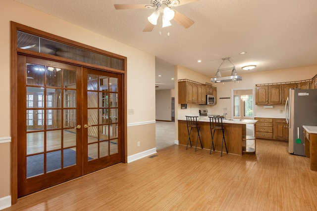 kitchen featuring ceiling fan, light hardwood / wood-style floors, kitchen peninsula, appliances with stainless steel finishes, and a kitchen bar