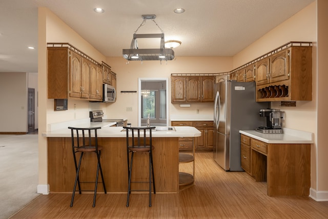 kitchen featuring sink, a breakfast bar area, kitchen peninsula, light hardwood / wood-style flooring, and stainless steel appliances