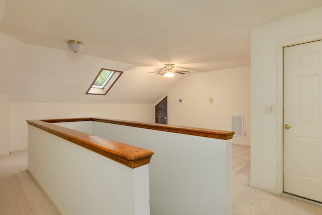 hall featuring a textured ceiling, vaulted ceiling with skylight, and light carpet