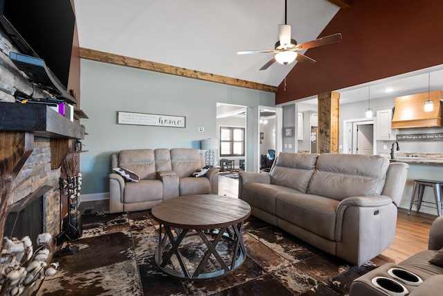 living room with ceiling fan, a stone fireplace, hardwood / wood-style floors, and high vaulted ceiling