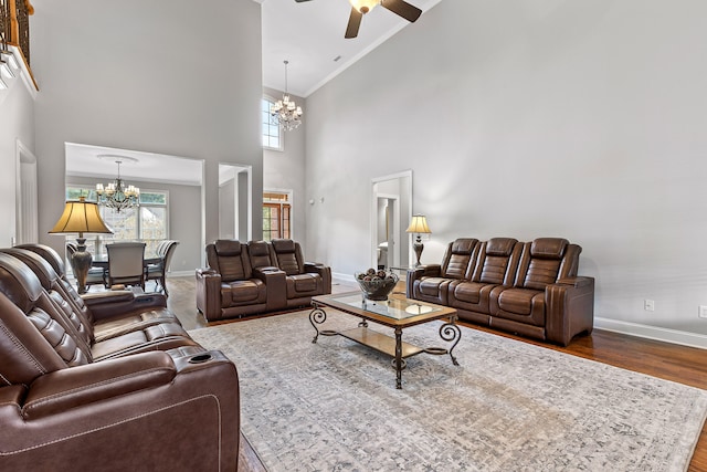 living room featuring ceiling fan with notable chandelier, wood-type flooring, ornamental molding, and a high ceiling