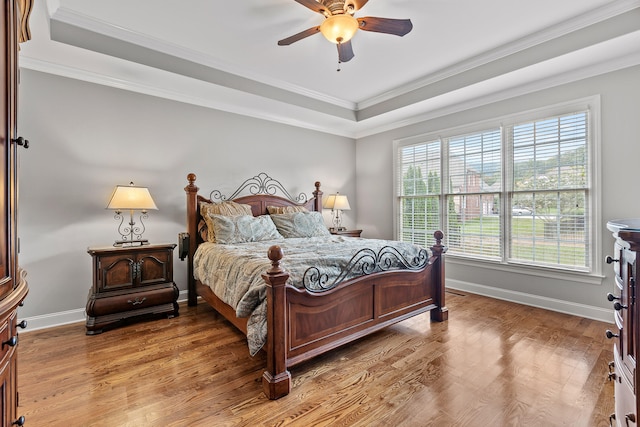 bedroom with hardwood / wood-style flooring, ceiling fan, a raised ceiling, and ornamental molding