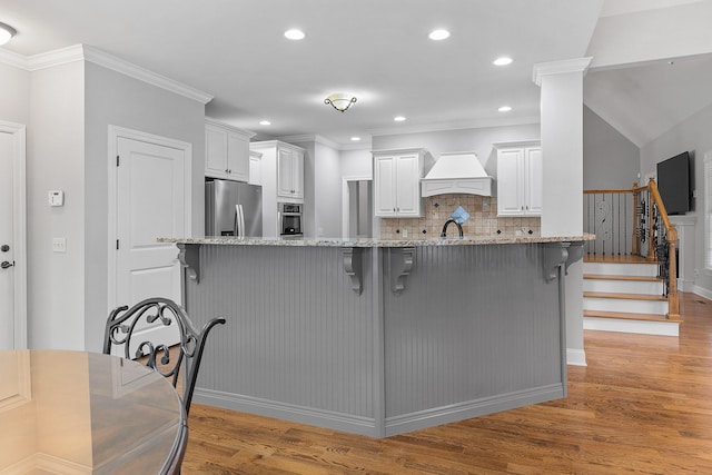 kitchen featuring a kitchen bar, light stone countertops, tasteful backsplash, stainless steel appliances, and white cabinetry