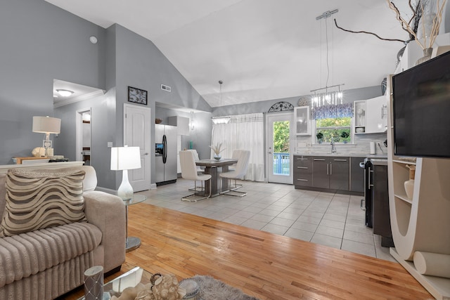 living room featuring sink, light wood-type flooring, a chandelier, and high vaulted ceiling