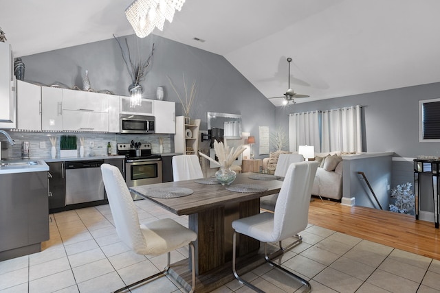 dining area featuring ceiling fan with notable chandelier, light wood-type flooring, vaulted ceiling, and sink