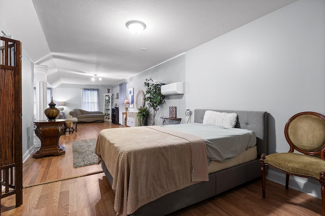 bedroom featuring an AC wall unit, vaulted ceiling, a textured ceiling, and hardwood / wood-style floors