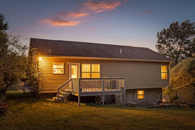 back house at dusk featuring a wooden deck and a yard