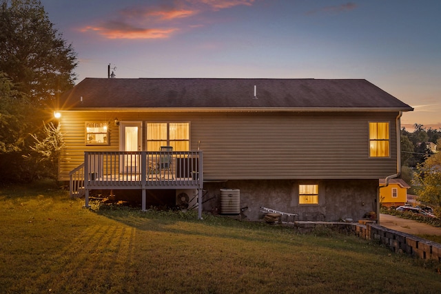 back house at dusk featuring a lawn, a wooden deck, and central air condition unit