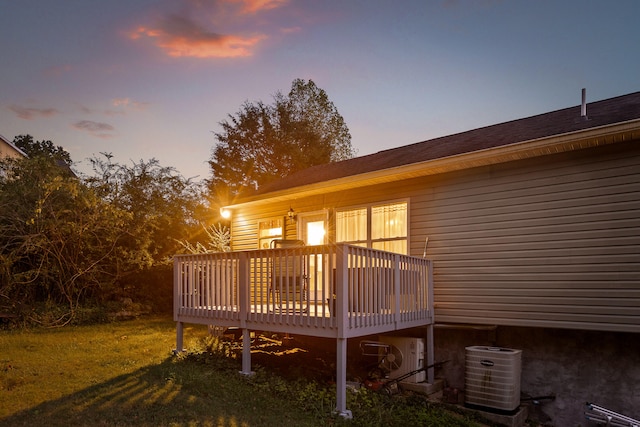 back house at dusk with a deck, a lawn, and central AC