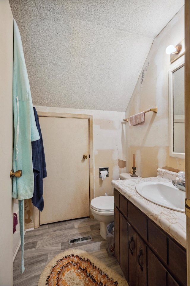 bathroom with lofted ceiling, vanity, hardwood / wood-style flooring, toilet, and a textured ceiling