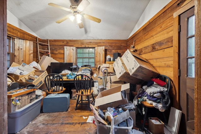 interior space featuring lofted ceiling, ceiling fan, wood-type flooring, wood walls, and a textured ceiling