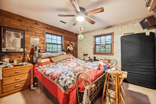 carpeted bedroom with wood walls, a textured ceiling, multiple windows, and ceiling fan