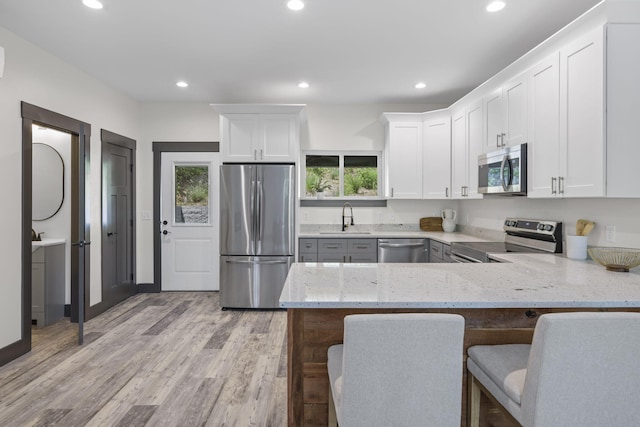 kitchen with kitchen peninsula, stainless steel appliances, a healthy amount of sunlight, sink, and light hardwood / wood-style floors