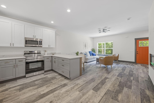 kitchen featuring light hardwood / wood-style flooring, kitchen peninsula, gray cabinets, white cabinets, and appliances with stainless steel finishes