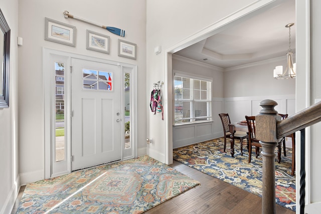 entryway with a raised ceiling, ornamental molding, a chandelier, and hardwood / wood-style flooring