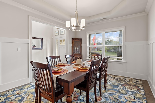 dining space with a raised ceiling, ornamental molding, hardwood / wood-style floors, and a notable chandelier