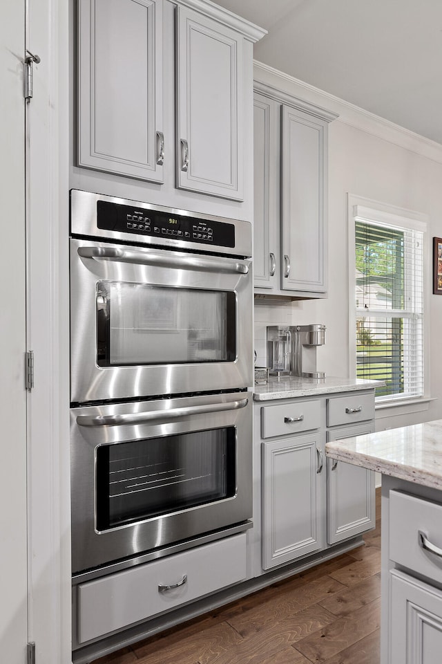 kitchen featuring gray cabinetry, light stone counters, dark hardwood / wood-style flooring, crown molding, and double oven