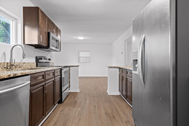 kitchen with dark brown cabinets, sink, light hardwood / wood-style flooring, stainless steel appliances, and light stone countertops