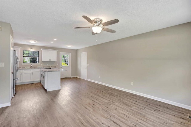 kitchen with stainless steel fridge, white cabinetry, a textured ceiling, light hardwood / wood-style flooring, and sink