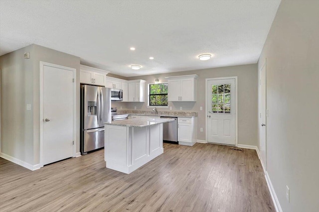 kitchen with light hardwood / wood-style floors, a textured ceiling, white cabinets, a kitchen island, and appliances with stainless steel finishes